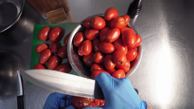 The chef, takes tomatoes from a bowl, cuts off the unusable parts of them