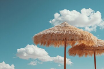 Fototapeta premium Two straw beach umbrellas against a bright blue sky with puffy white clouds