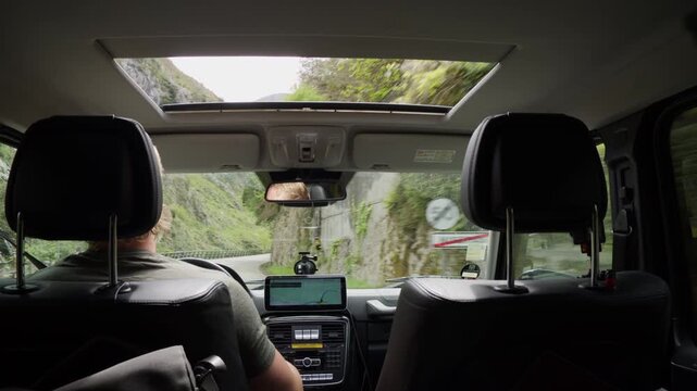 Backseat point of view of a driver navigating narrow road through a mountain gorge. Scenic travel with green nature and rocky cliffs