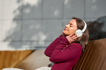 Relaxed Woman Enjoying Music With White Headphones On Outdoor Bench In Sunlight