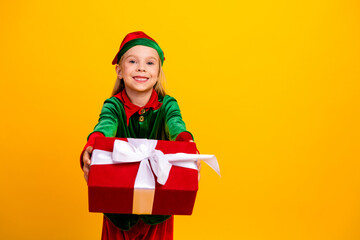 Excited little elf child offering a cheerful Christmas gift with a big smile, set against a bright festive yellow background