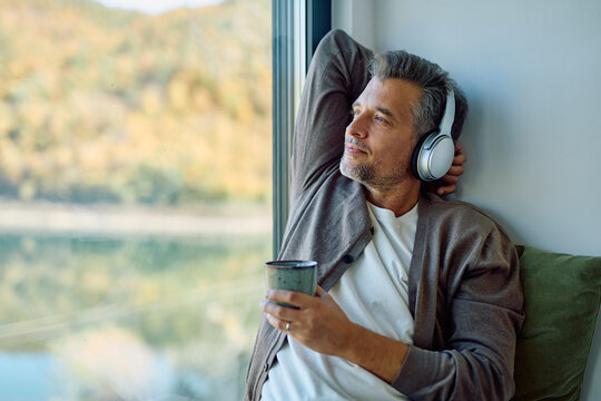 Mature man enjoying a peaceful moment, wearing headphones and drinking coffee while looking at the autumn lake view - Powered by Adobe