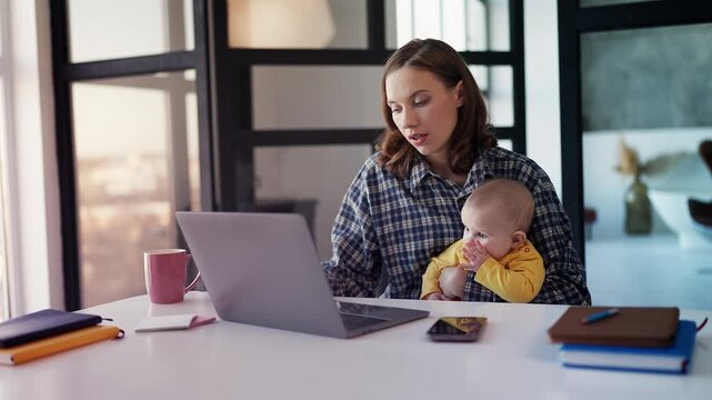 Tired single mom finishing work on laptop while holding baby, stress at home
