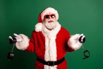 Santa in red suit with fur trim and hat presents a playful festive image with handcuffs against a green background for holiday promotion