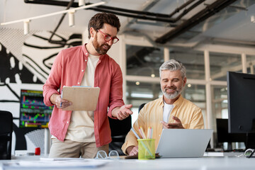 Handsome bearded men wearing stylish casual clothes working together in modern office using laptop