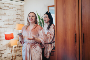 Two women dressed in robes enjoy a comfortable moment together in a home setting. The warm lighting...
