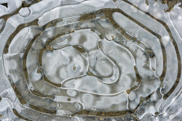 Intricate patterns of ice are visible on a surface, showcasing unique shapes and textures. This natural artwork forms during cold winter months near a frozen lake, highlighting seasonal changes.