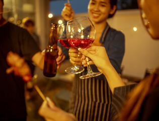 An Asian woman and friends toast with wine during a cozy backyard BBQ. Grilling skewers over charcoal under string lights, they celebrate friendship, joy,  togetherness in a festive outdoor evening