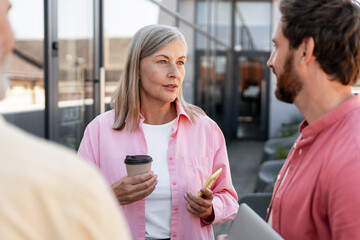 Smiling gray haired woman holding coffee cup relaxing talking with bearded man outdoor on the street