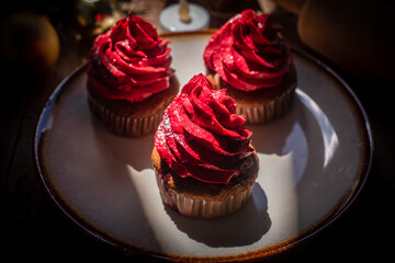 Delicious chocolate cupcakes topped with red buttercream, served on a ceramic plate with a warm festive atmosphere. Perfect sweet dessert for Christmas and New Year celebration.