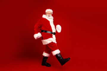 Santa Claus in a classic red suit with white fur trim walking forward against a bright red holiday backdrop for a Christmas themed stock photo