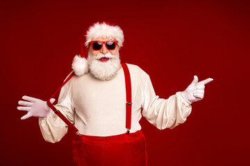 Santa in red suit with sunglass and suspenders posing against a red backdrop for Christmas holiday promotion