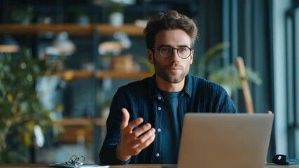 Confident male freelancer communicates online, gesturing while speaking at his desk in a stylish, sunlit office. Contemporary interior design and natural elements create a productive atmosphere - Powered by Adobe