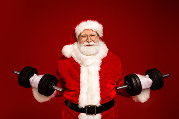 Santa lifts heavy dumbbells in a festive red studio for a humorous fitness themed Christmas image for holiday promotions