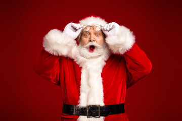 Santa Claus surprises with glasses as he poses in a vibrant red studio backdrop for a festive...