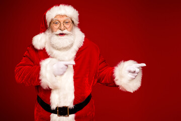 Santa Claus in red suit with white fur points playfully against a bold red background for a festive holiday season image