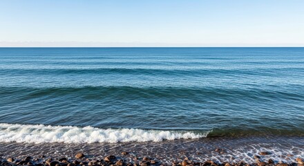 Tranquil ocean waves gently crashing on rocky shoreline under clear blue sky