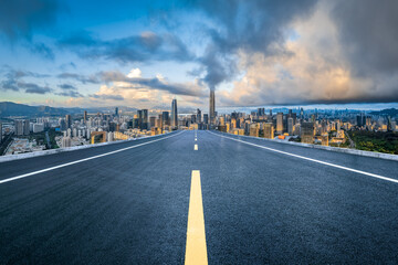 Empty asphalt road leading to a modern city skyline with commercial buildings under a dramatic...