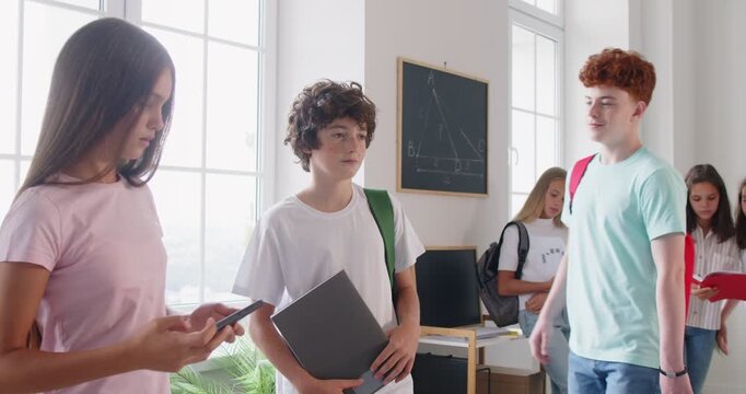 Teenage girl taking video on mobile phone camera of school boy bullying his classmate standing in the classroom. Stressed student bullied by aggressive pupil. 4k video. Slow motion video.