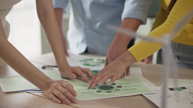 Close-up shot of diverse team members reviewing, pointing at green ESG project documents during a collaborative meeting. Focus on charts and data related to climate action and sustainability.