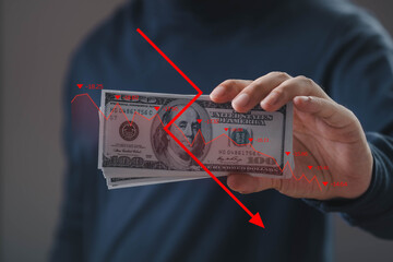 Hand holding US dollar bills with red downward graph overlay, symbolizing financial loss, economic...