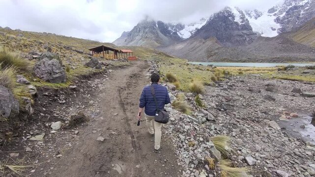 Follow from behind as TV host Charles Huang walks past a rest area structure and arrives at Pata Cocha Lake in the Ausangate region