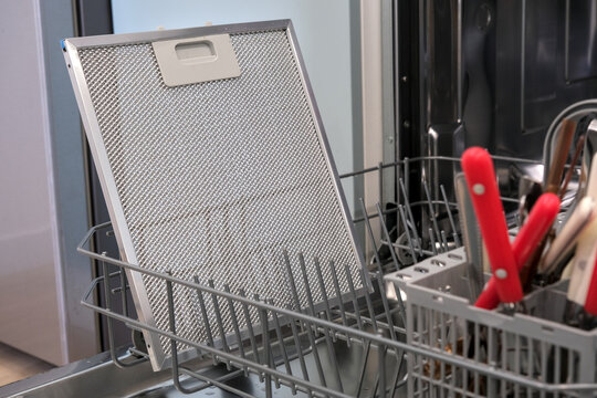 Range hood grease filter placed in dishwasher for easy cleaning, showing practical maintenance of kitchen equipment in a modern home.