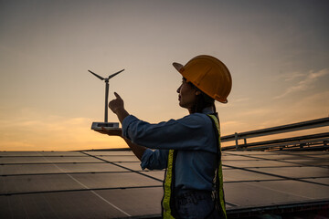 A woman wearing a hard hat and safety vest is pointing to a wind turbine. Concept of innovation and progress in the field of renewable energy © KANGWANS