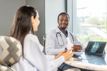In a hospital, male and female medics discuss human skeleton anatomy. They use a tablet and a model bone to explain the structure of bones and joints, sharing knowledge with enthusiasm.