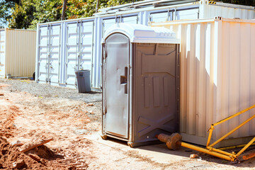 Portable restroom is located next to shipping containers at busy construction area