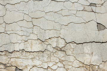 Weathered cracked wall displays distressed texture under bright daylight. Grungy appearance evokes a sense of age and decay in the outdoor setting.