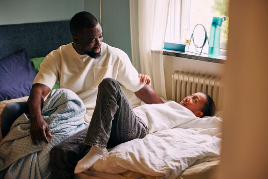 Father talking with son lying on bed in bedroom at home