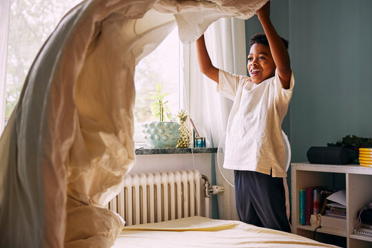 Happy boy spreading sheet on bed in bedroom at home