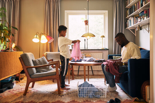 Boy helping father sitting on sofa while folding clothes at home