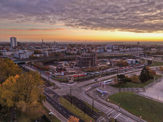 Aerial view of the city of Rostock at sunset highlighting a major construction site surrounded by roads, traffic, and residential buildings under a colorful evening sky