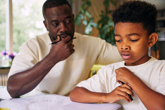 Focused boy studying with help of father at home