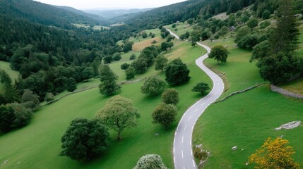 Aerial View Of A Winding Highway Road Cutting Through A Lush Green Valley With Rolling Hills And Scattered Trees Under A Cloudy Sky