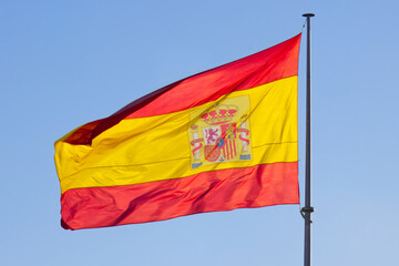 Spanish flag waving in the strong wind against a clear blue sky.