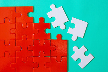 Fototapeta premium Unfinished red jigsaw puzzle pieces and three pieces white jigsaw puzzle on blue background 