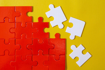 Unfinished red jigsaw puzzle pieces and three pieces white jigsaw puzzle on yellow background 