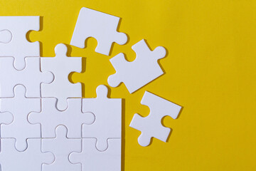 Unfinished white jigsaw puzzle pieces on yellow background