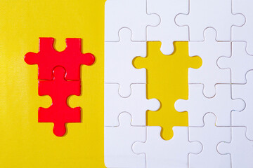 Fototapeta premium two red elements from jigsaw puzzle and unfinished white jigsaw puzzle on yellow background. 