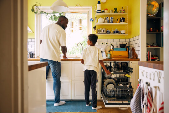 Rear view of son helping father in washing utensils inside dishwasher at home