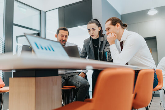 A diverse team of professionals collaborates around a laptop in a bright, modern office, reviewing charts and discussing strategy.
