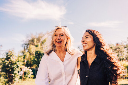 Happy senior woman walking with arm around daughter in back yard