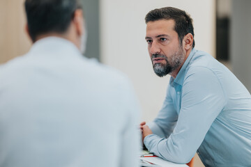 Colleagues sit across from each other in a modern office, deeply engaged in a discussion. The man...