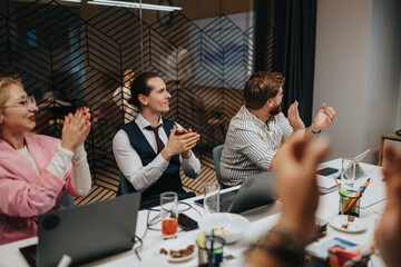 Colleagues sit around a conference table, clapping and smiling as they celebrate an achievement. The scene features laptops, drinks, snacks, and a stylish patterned divider in the background.