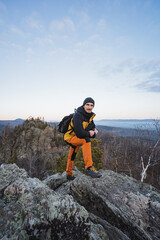 Individual exploring mountain peak during sunset, Adventurer standing on rugged summit with panoramic views at golden hour, Lone trekker surveying crisp autumn scenery from rocky height