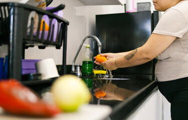 Colombian woman washing vegetables in kitchen sink, getting ready to cook family meal