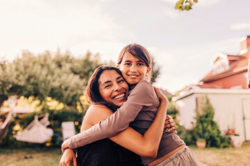 Portrait of smiling affectionate mother embracing daughter in garden